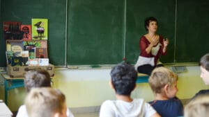 Une dame assise devant un tableau noir raconte des histoires à une classe d'enfants.