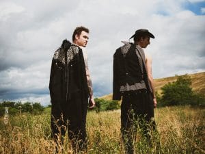 Deux hommes se trouvent de dos au milieu d'un champs vêtus de costumes de cow-boys.